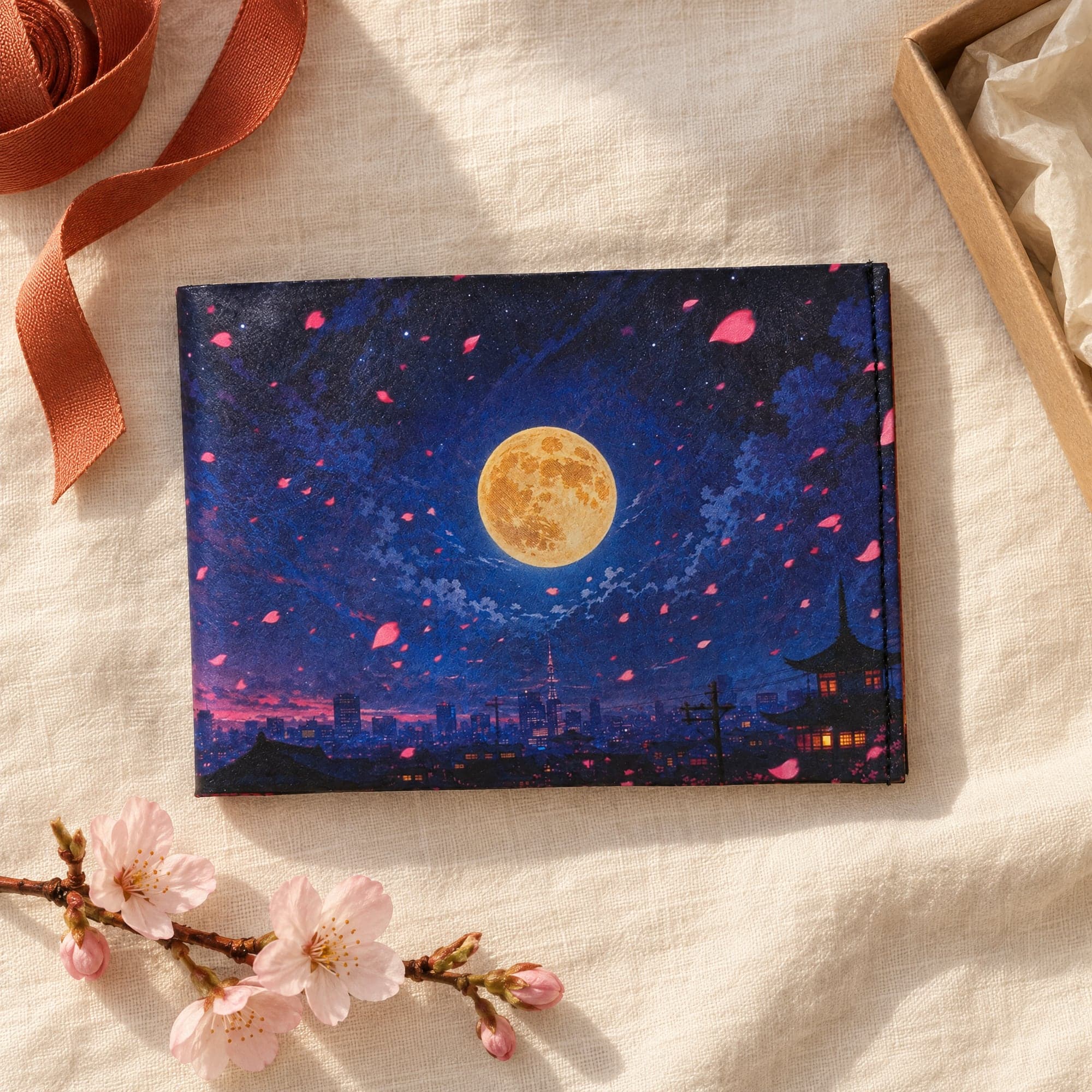 Anime Hero wallet on cream linen beside a kraft gift box, with a sprig of cherry blossom