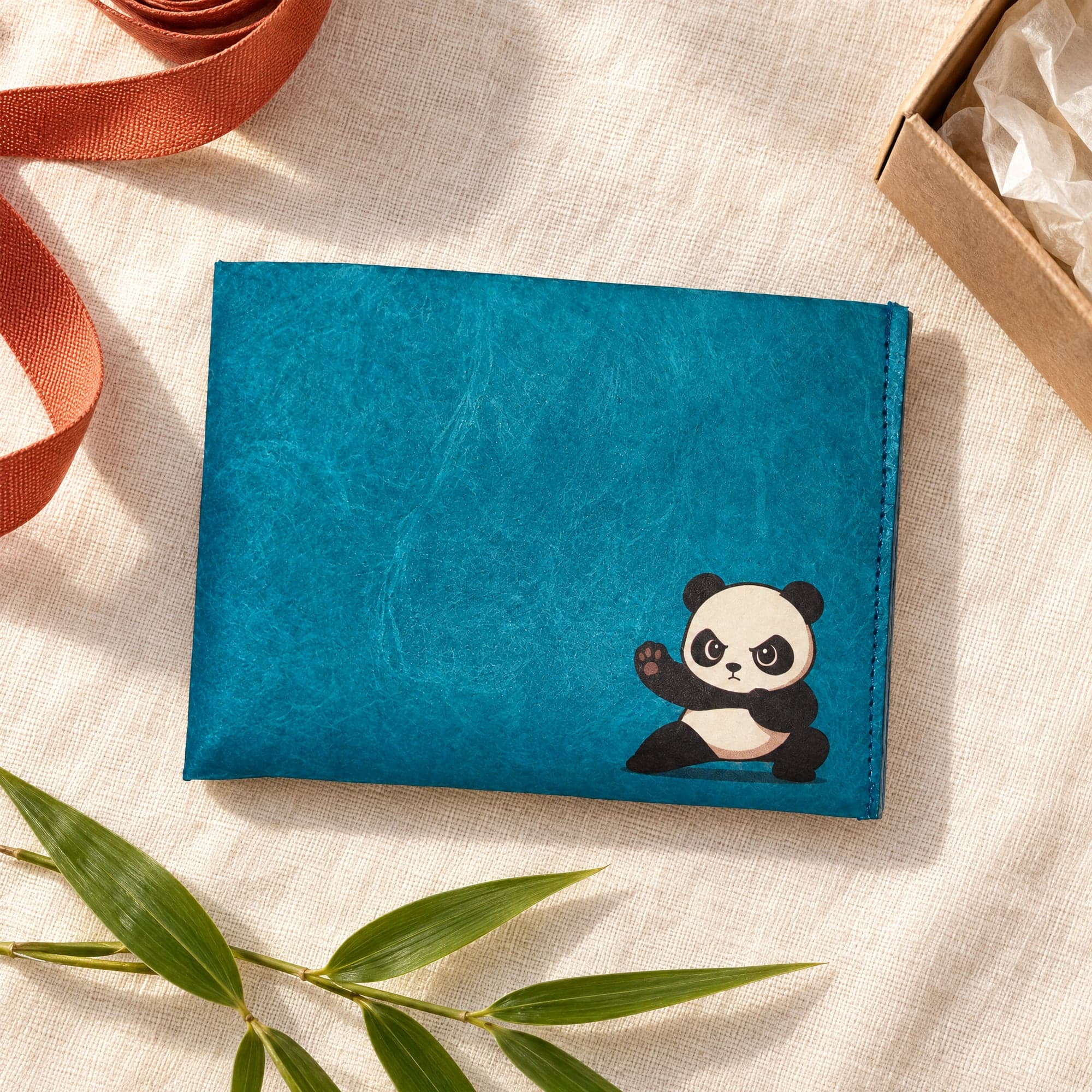 Cute Panda wallet on cream linen beside a kraft gift box, with a sprig of bamboo